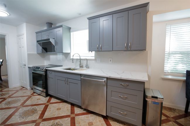 Kitchen with stainless steel appliances, gray cabinets, light stone counters, range hood, and inlaid floor details | Image 12