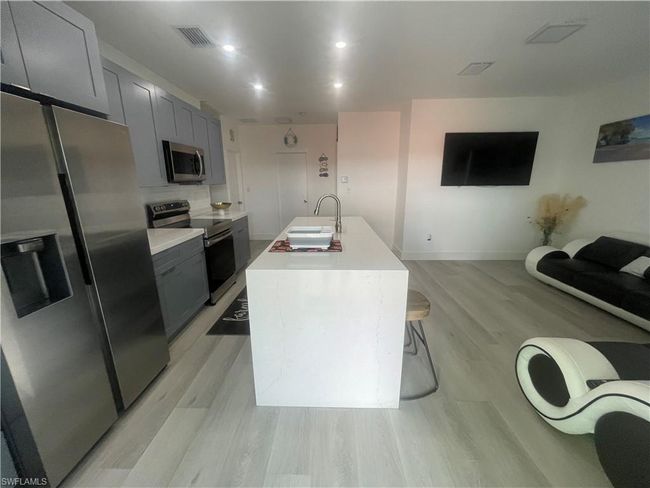 Kitchen with light wood-type flooring, appliances with stainless steel finishes, an island with sink, gray cabinets, and sink | Image 3