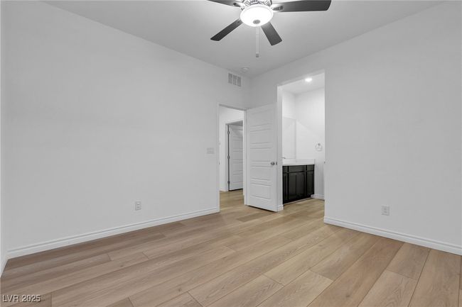 Unfurnished bedroom featuring light wood-style flooring, baseboards, ensuite bathroom, and ceiling fan | Image 16