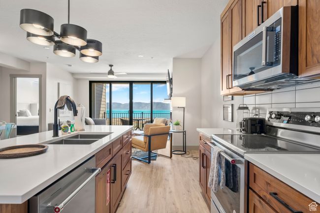 Kitchen with appliances with stainless steel finishes, a sink, brown cabinetry, open floor plan, and light wood-style floors | Image 60