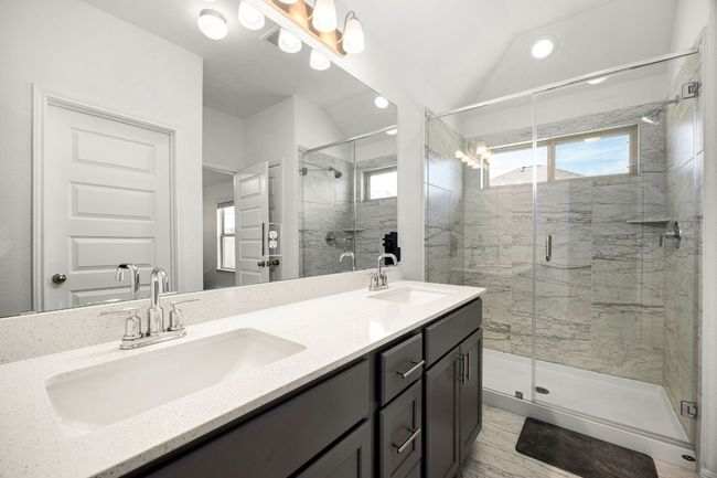 Bathroom featuring healthy amount of natural light, double vanity, a stall shower, marble finish flooring, and vaulted ceiling | Image 22
