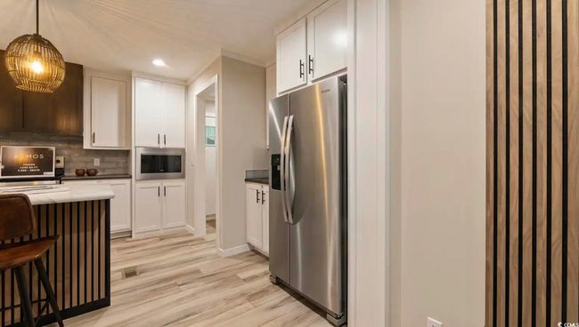Kitchen featuring appliances with stainless steel finishes, a breakfast bar, tasteful backsplash, light wood finished floors, and white cabinetry | Image 9