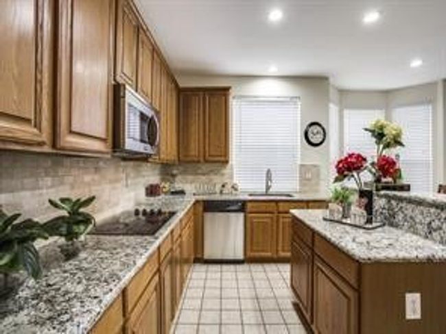 Kitchen with appliances with stainless steel finishes, brown cabinetry, decorative backsplash, recessed lighting, and light tile patterned flooring | Image 9