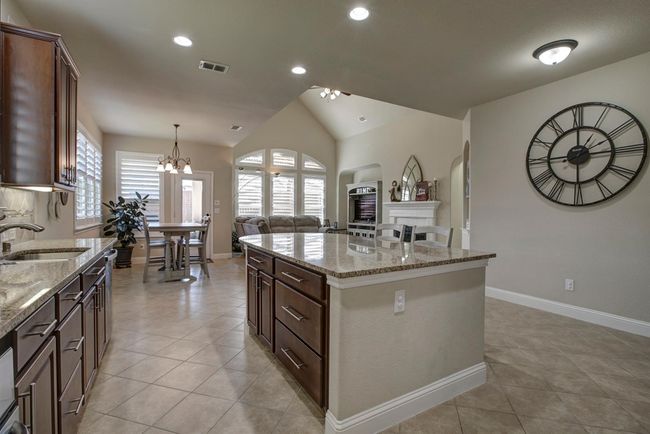Kitchen with light tile patterned floors, a chandelier, vaulted ceiling, light stone countertops, and open floor plan | Image 8