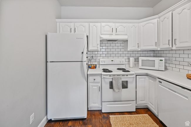 Kitchen with white cabinets, dark hardwood / wood-style flooring, white appliances, and tasteful backsplash | Image 6