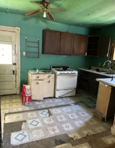 Kitchen featuring sink, light tile patterned flooring, white range with gas stovetop, and ceiling fan | Image 2