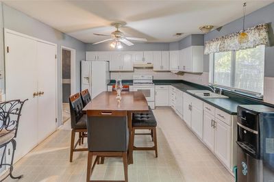 Kitchen featuring a kitchen island, a breakfast bar, white cabinetry, sink, and white appliances | Image 3