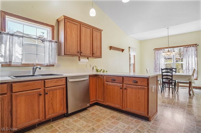 Kitchen featuring a peninsula, stainless steel dishwasher, a sink, lofted ceiling, and brown cabinetry | Image 21