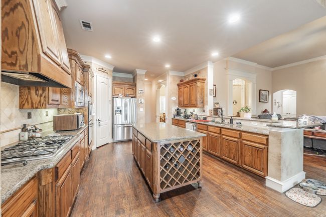Kitchen with stainless steel appliances, arched walkways, crown molding, dark wood-type flooring, and light stone countertops | Image 18