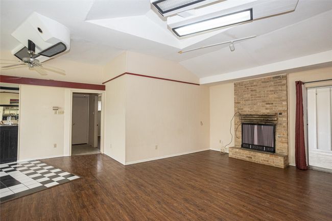 Another view of living room featuring wood finished floors, vaulted ceiling, a brick fireplace, and ceiling fan | Image 6