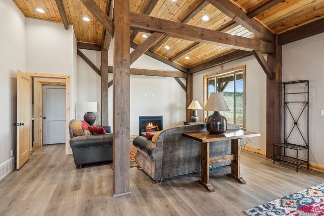 Living room featuring wood ceiling, beam ceiling, light wood-type flooring, and a lit fireplace | Image 39