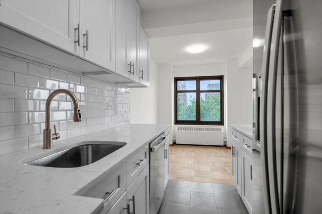 Kitchen featuring appliances with stainless steel finishes, decorative backsplash, radiator, light stone counters, and white cabinetry | Image 6