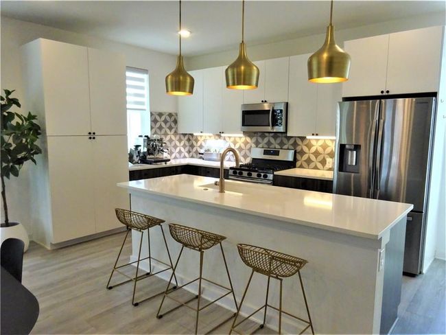 Kitchen featuring stainless steel appliances, decorative backsplash, a breakfast bar, and white cabinets | Image 4
