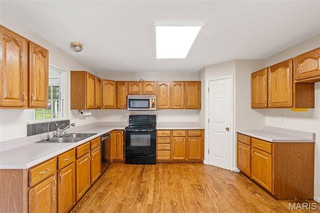 Kitchen featuring appliances with stainless steel finishes, a sink, light wood-style floors, light countertops, and brown cabinetry | Image 7