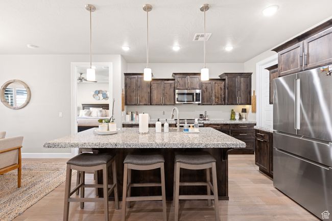Kitchen with appliances with stainless steel finishes, dark brown cabinets, a kitchen bar, light wood-style floors, and recessed lighting | Image 50