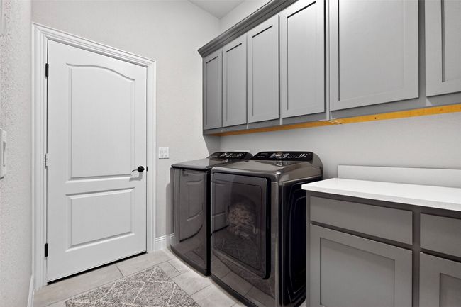 Laundry room featuring cabinet space, washer and dryer, light tile patterned floors, and baseboards | Image 32