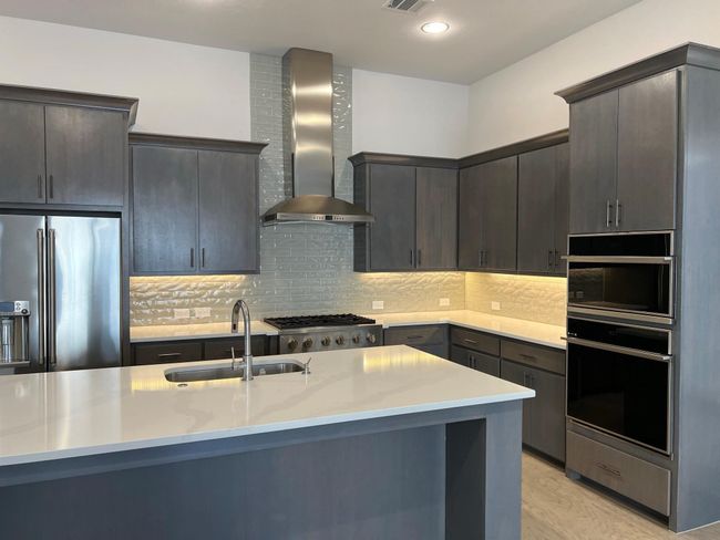 Kitchen featuring oven, wall chimney range hood, stainless steel fridge, a sink, and light countertops | Image 4