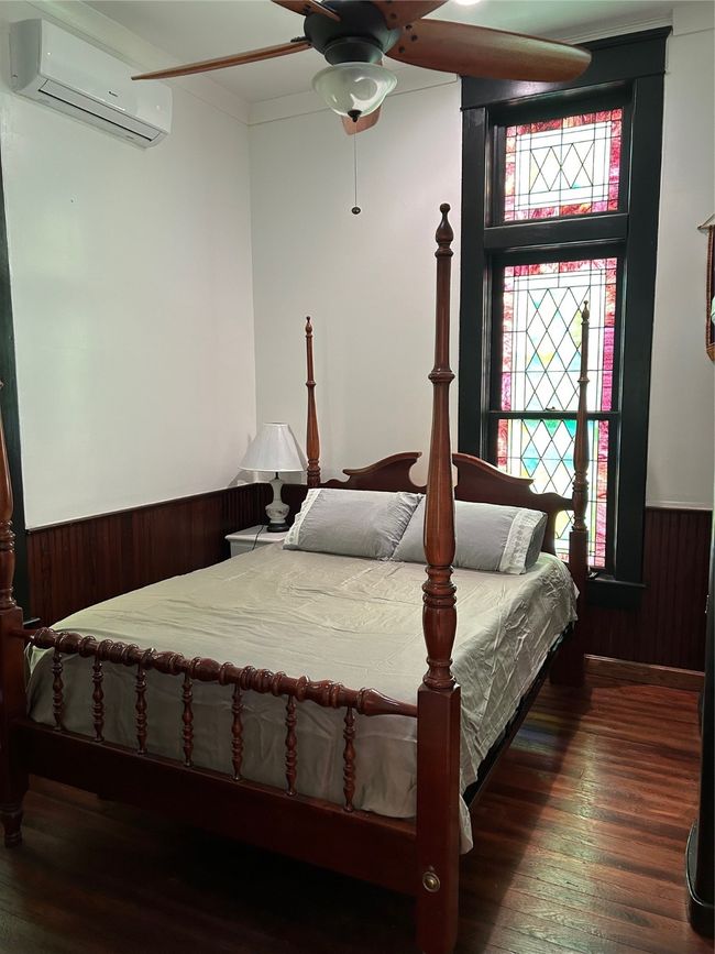 Bedroom with wainscoting, wooden walls, a wall mounted air conditioner, ceiling fan, and dark wood-type flooring | Image 17