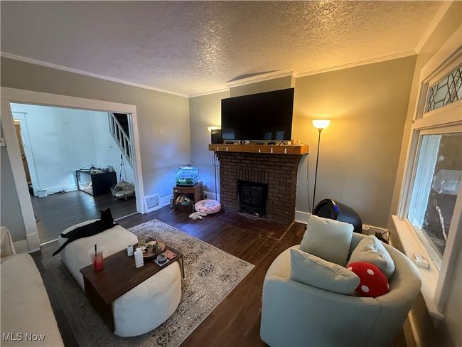 Living room with visible vents, a textured ceiling, wood finished floors, and ornamental molding | Image 5