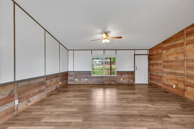 Empty room featuring wood walls, a ceiling fan, wood finished floors, a textured ceiling, and vaulted ceiling | Image 10