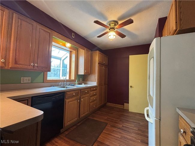 Kitchen featuring black dishwasher, dark wood finished floors, a sink, and freestanding refrigerator | Image 4