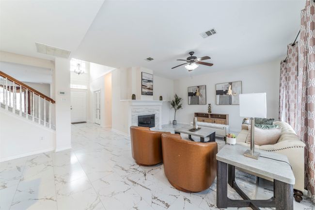 Living area featuring a ceiling fan, stairway, a glass covered fireplace, marble finish flooring, and a chandelier | Image 5