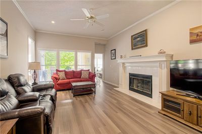 Living room with a textured ceiling, a tiled fireplace, light hardwood / wood-style flooring, ornamental molding, and ceiling fan | Image 2