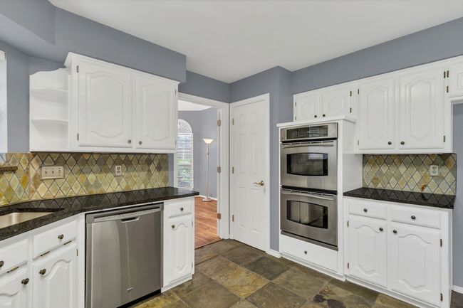 Kitchen with stainless steel appliances, dark countertops, white cabinets, open shelves, and backsplash | Image 15