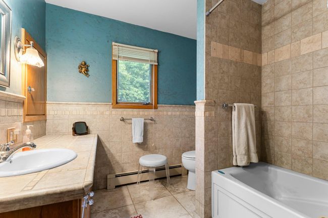 A full bathroom serves this level, complete with tiled floors, a large single vanity with tiled counters, and a jetted tub/shower combo. A nearby hall closet offers extra storage for linens and more. | Image 8