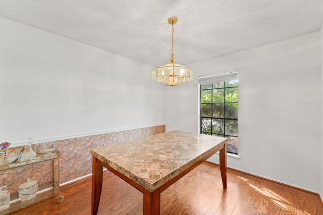 Bright dining area with a marble-top table, elegant chandelier, and large window providing natural light. Wood flooring adds warmth to the space. | Image 11