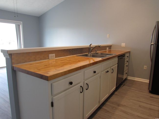 Kitchen featuring a peninsula with butcher block counter tops, white cabinets, double bay sink and stainless steel appliances. | Image 21