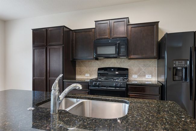 Kitchen with black appliances, a sink, dark brown cabinets, tasteful backsplash, and dark stone countertops | Image 8