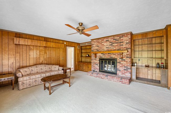 Carpeted living room with wooden walls, ceiling fan, a brick fireplace, and built in shelves | Image 15