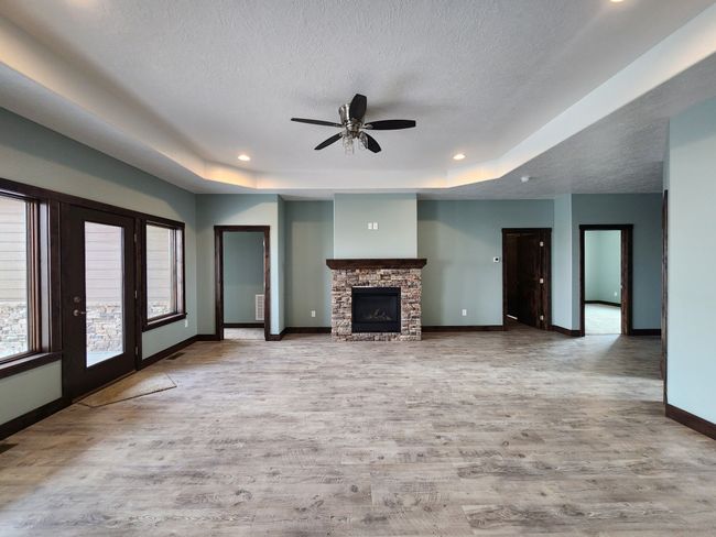 Unfurnished living room featuring a raised ceiling, wood finished floors, a ceiling fan, a stone fireplace, and a textured ceiling | Image 4