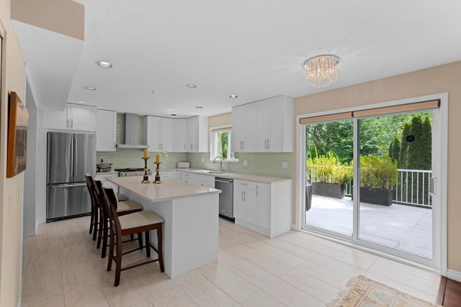 Kitchen featuring stainless steel appliances, wall chimney range hood, a breakfast bar area, light countertops, and decorative backsplash | Image 8