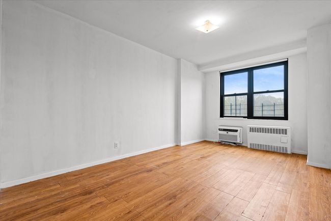 Empty room featuring an AC wall unit, baseboards, radiator heating unit, and light wood-style flooring | Image 10