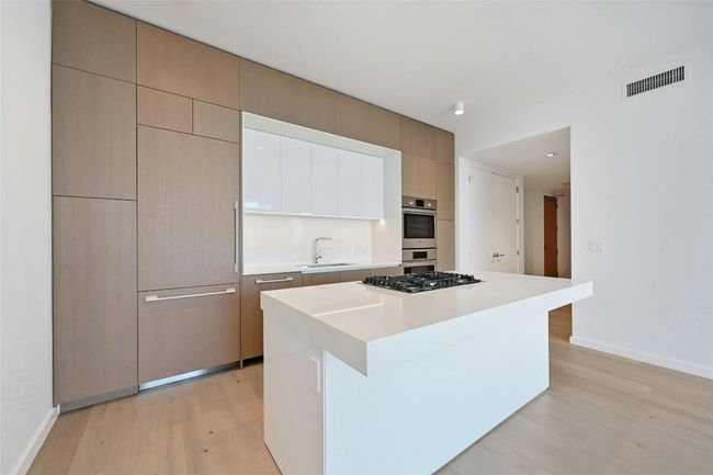 A streamlined culinary space highlighted by Bosch appliances, a gas cooktop built into the expansive quartz island, and custom cabinetry that seamlessly conceals the refrigerator and dishwasher for a clean, modern aesthetic. | Image 5