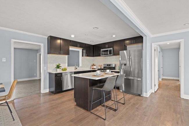 Kitchen featuring light wood-style flooring, stainless steel appliances, light countertops, and ornamental molding | Image 11