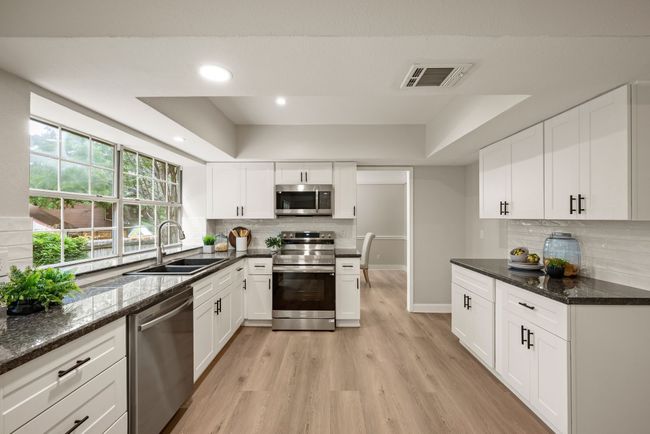 The white cabinetry, black hardware, granite countertops, and stainless steel appliances create a fresh, modern aesthetic. | Image 14