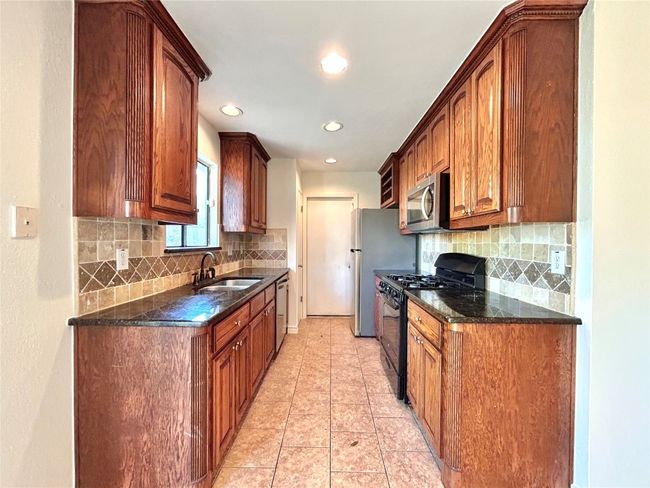 Kitchen featuring stainless steel appliances, backsplash, recessed lighting, light tile patterned flooring, and dark stone countertops | Image 7
