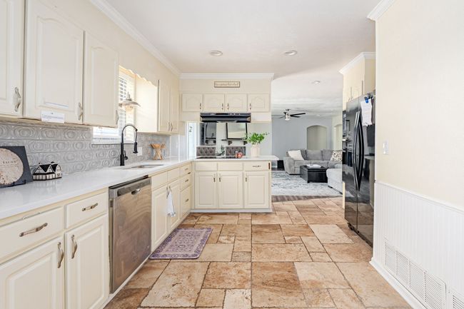 Kitchen featuring stainless steel dishwasher, black refrigerator with ice dispenser, ceiling fan, a sink, and decorative backsplash | Image 23