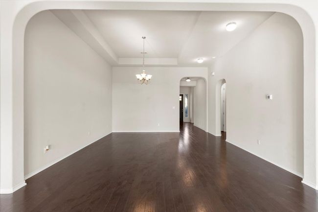 Spare room with arched walkways, dark wood-style floors, a chandelier, and a tray ceiling | Image 4