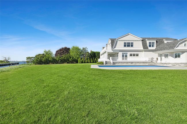 Rear view of house with a gambrel roof, a lawn, an outdoor pool, a water view, and a patio | Image 47