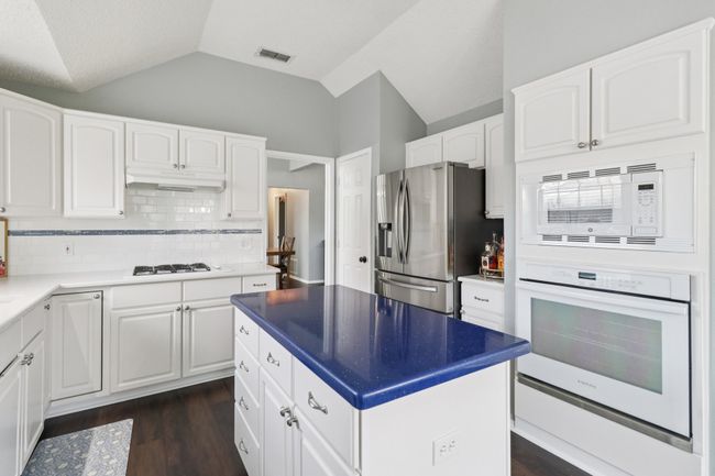 Kitchen featuring white appliances, lofted ceiling, under cabinet range hood, decorative backsplash, and white cabinetry | Image 13
