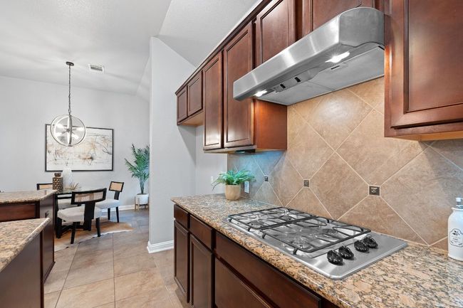Kitchen with under cabinet range hood, stainless steel gas cooktop, tasteful backsplash, and a chandelier | Image 15