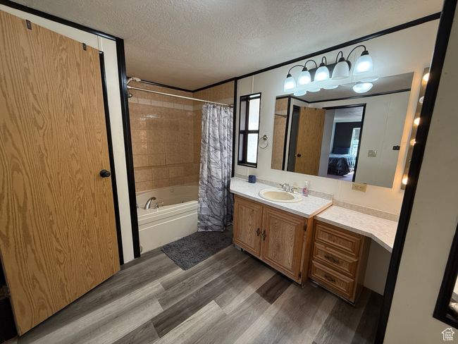 Ensuite bathroom featuring a textured ceiling, wood finished floors, shower / bath combo with shower curtain, and vanity | Image 9