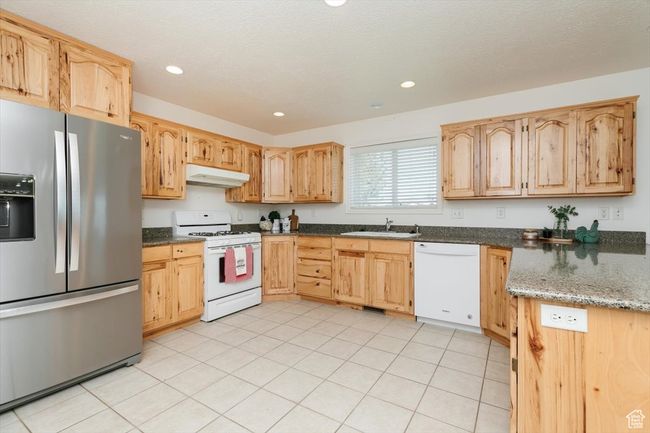 Kitchen with white appliances, under cabinet range hood, light brown cabinets, dark stone countertops, and recessed lighting | Image 37