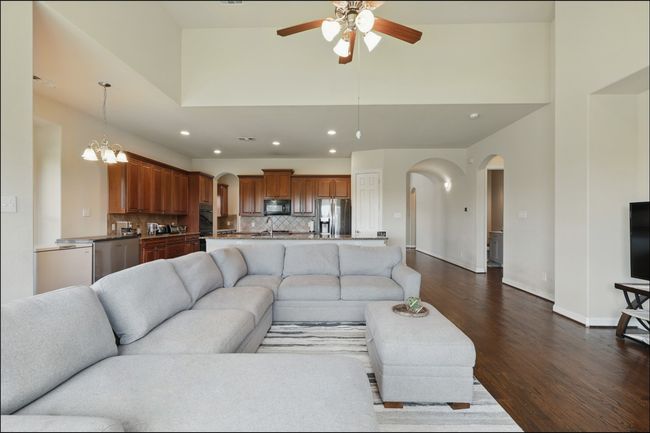 Living area featuring dark wood finished floors, ceiling fan, a stone fireplace, and high vaulted ceiling | Image 16