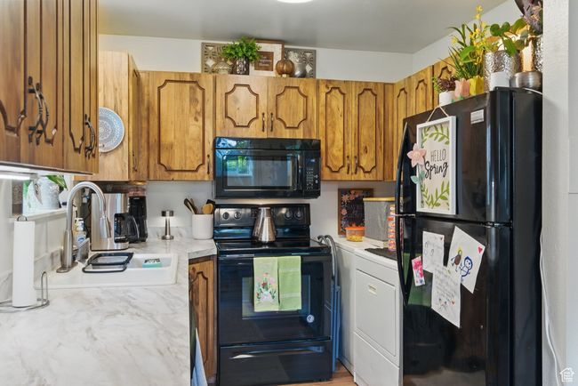 Kitchen with a sink, black appliances, brown cabinets, light countertops, and washer / clothes dryer | Image 40