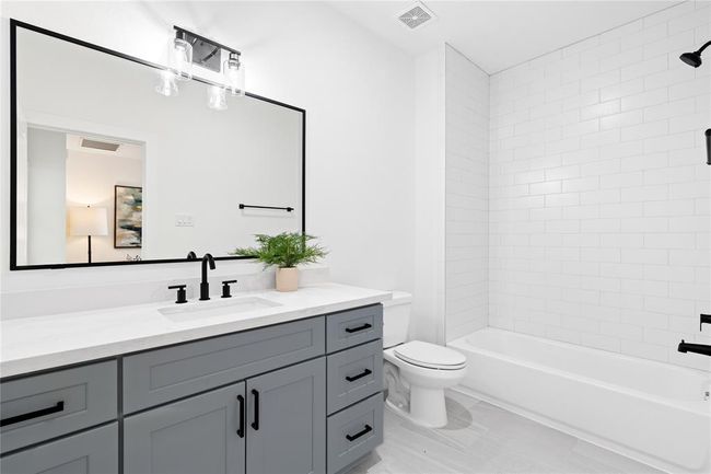 Designed with a contemporary aesthetic, this bathroom features a stylish gray vanity with black hardware and a crisp white quartz countertop. | Image 25